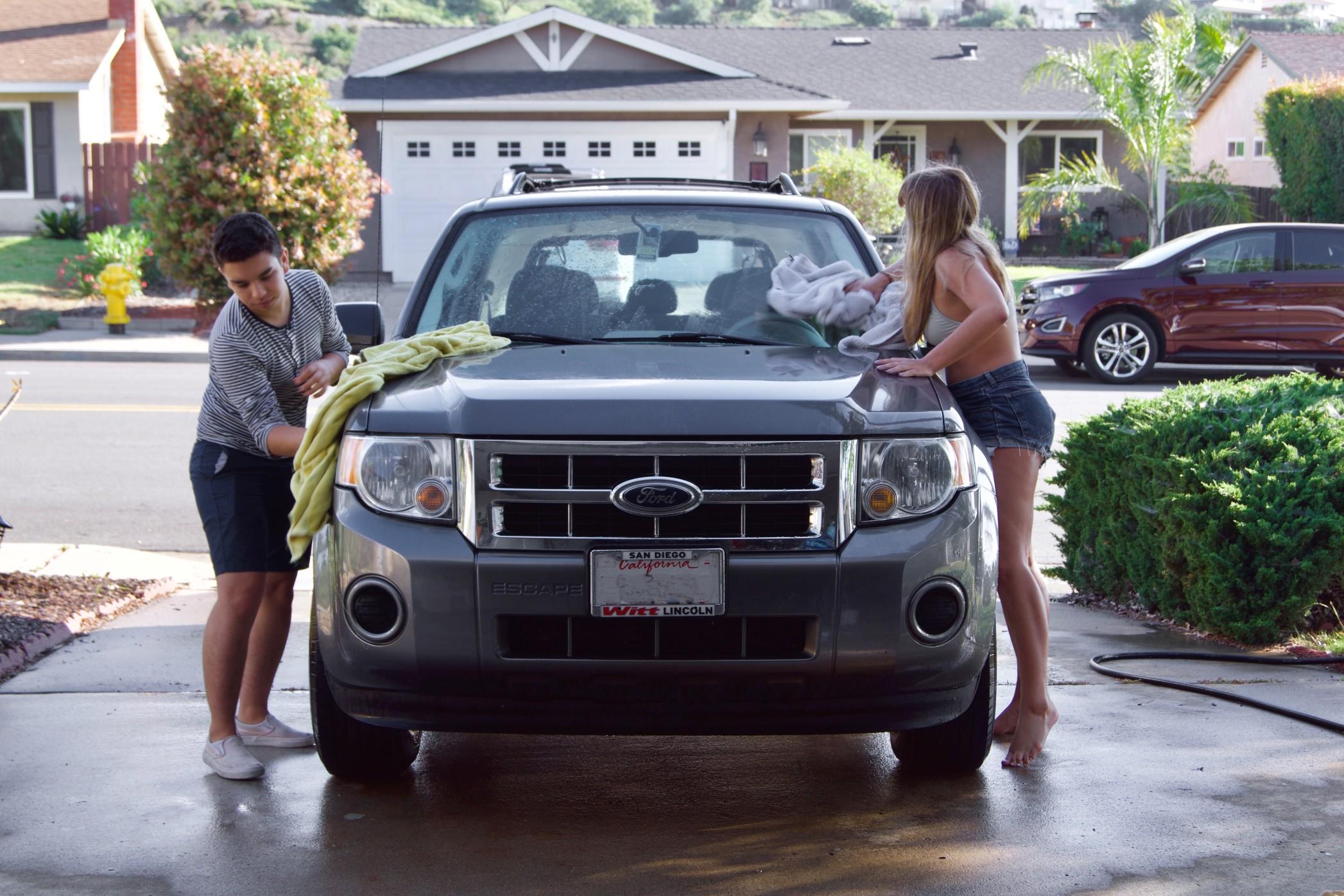 Two people washing their car in a driveway.