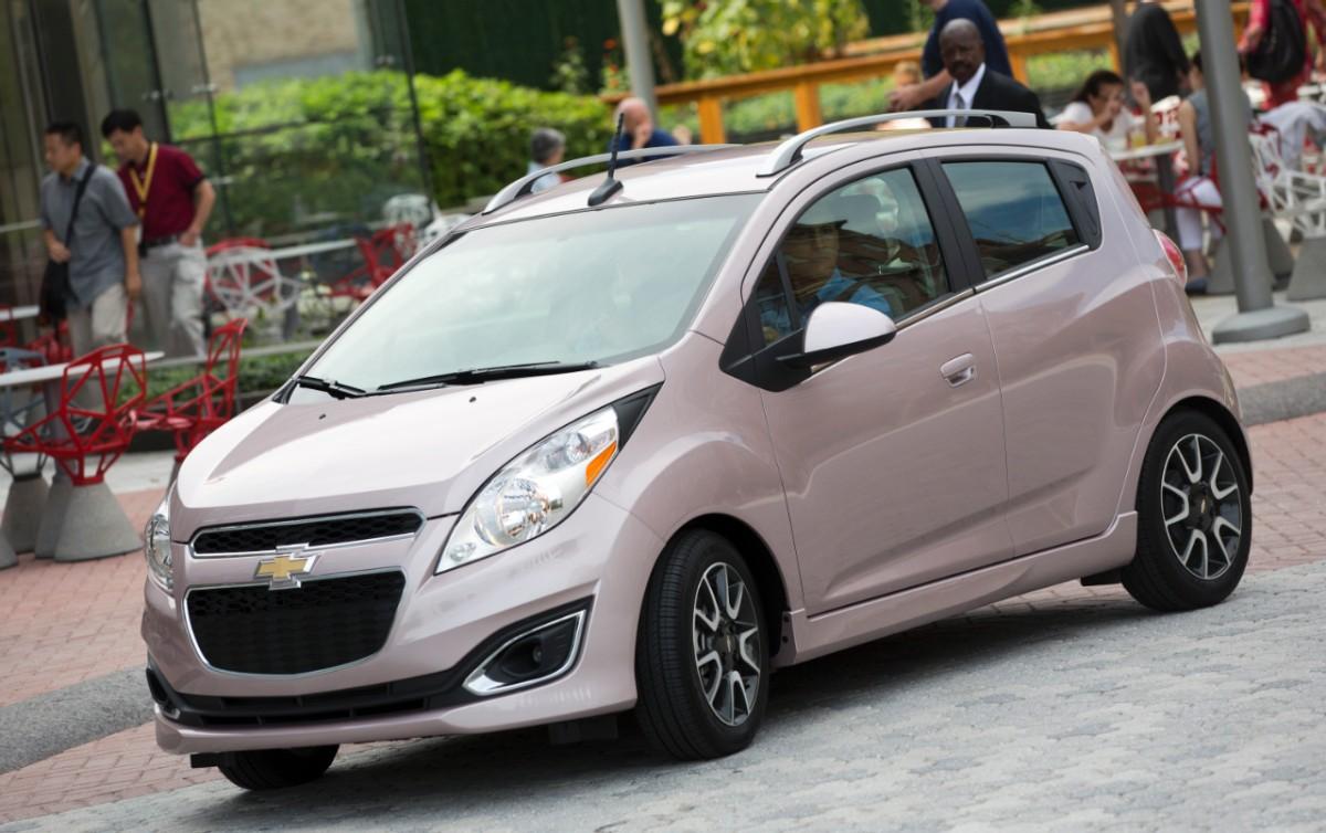 A pink 2013 Chevrolet Spark driving down a street. 