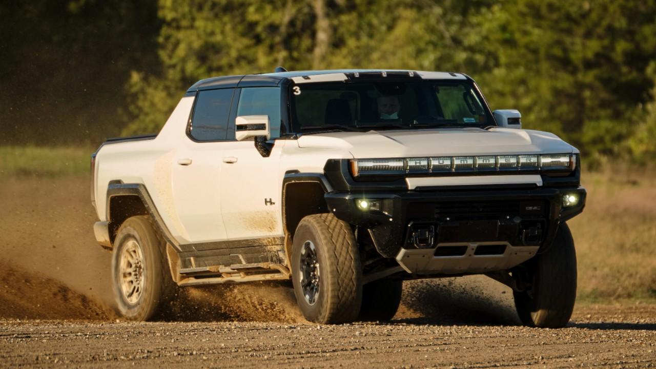 A white Hummer electric truck driving down a dusty dirt road.