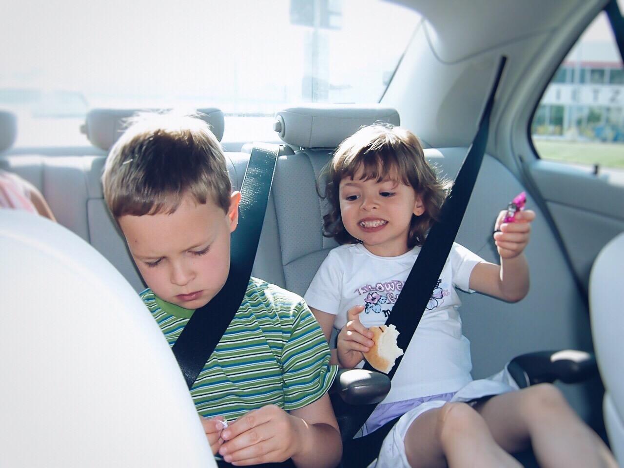 Two children in the backseat of a car, with one of them in a booster seat.