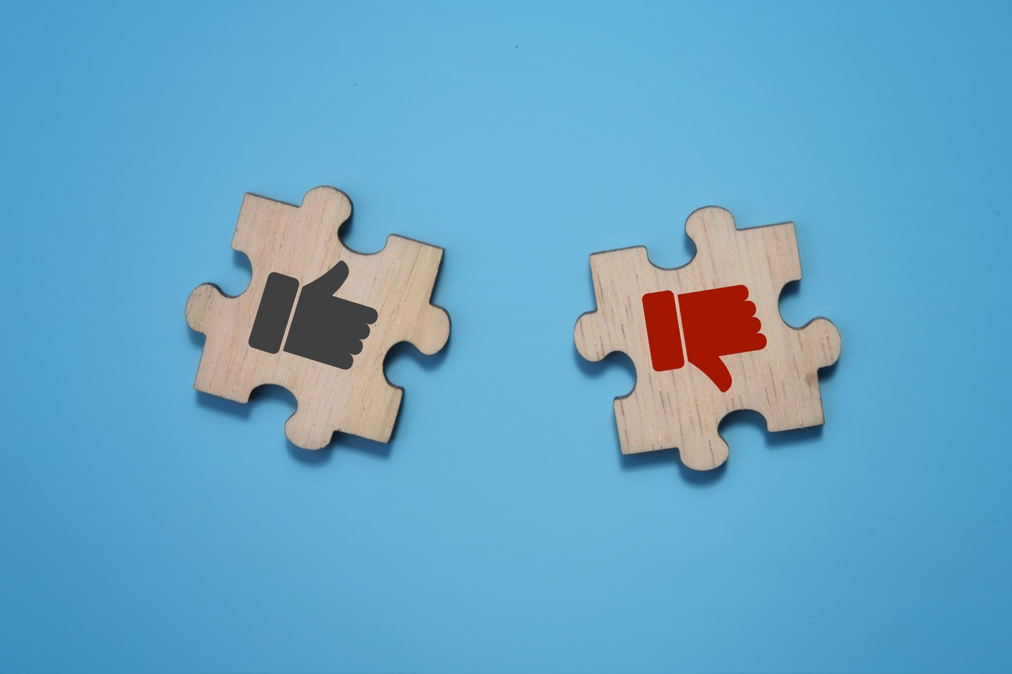 A black thumbs-up symbol and a red thumbs-down in two wood puzzle pieces on a blue background