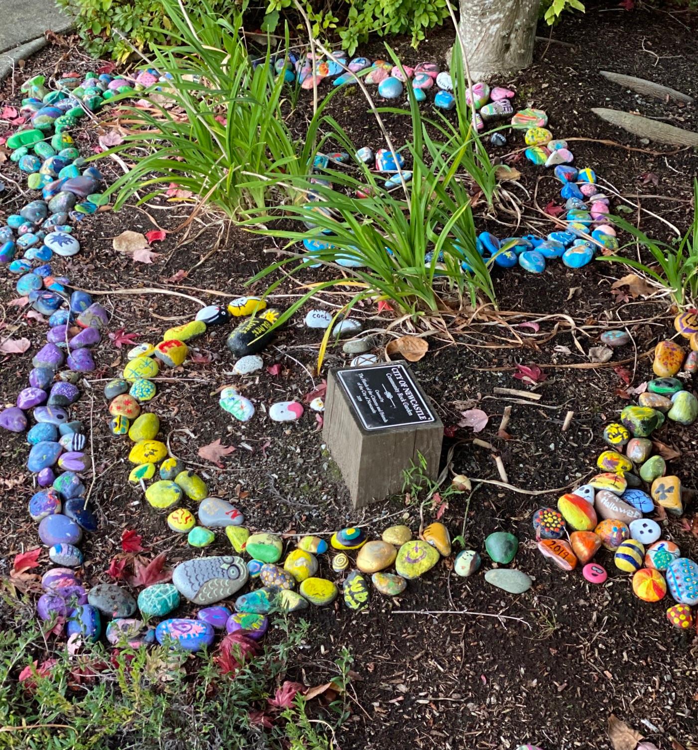 Multicolored stone designs decorate a garden of dark mulch and plants.