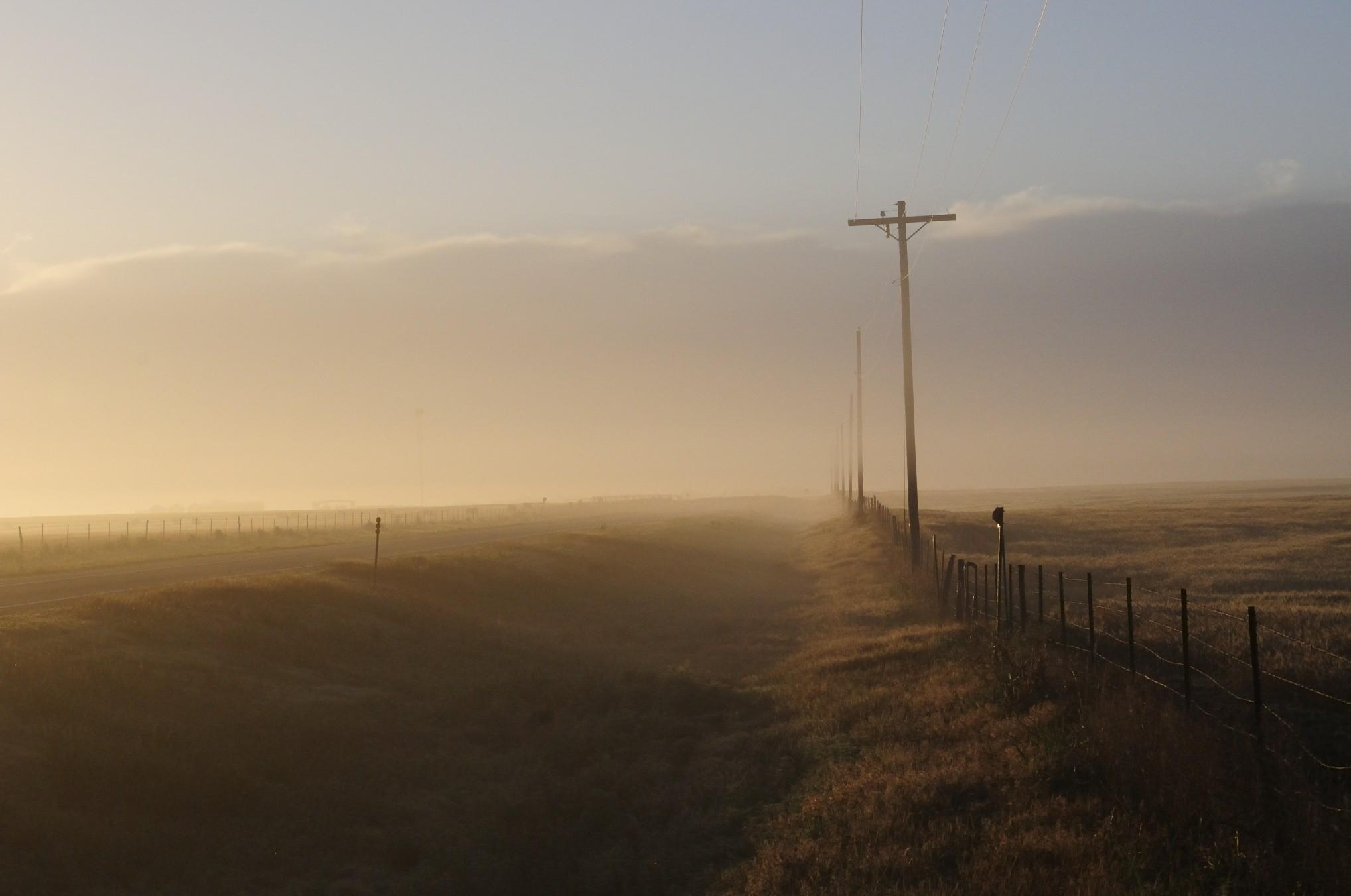 View of a field and a road on a foggy morning in rural Oklahoma. 