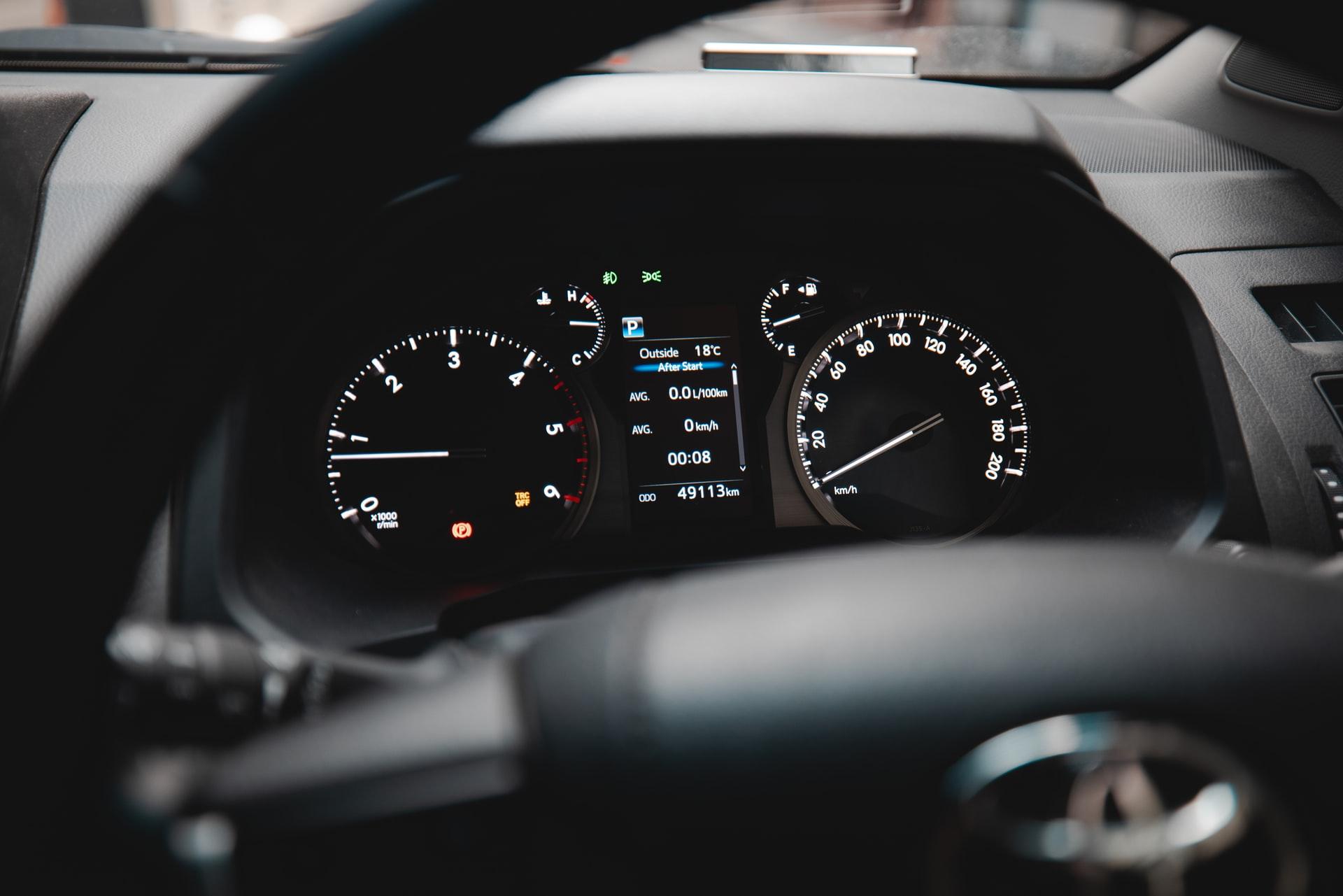 Black wheel and dash of a Toyota with lit-up speedometer
